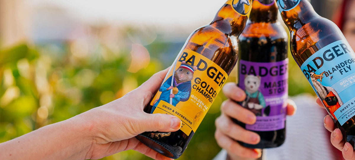 Hands passing bottles of Badger ale beside a plate of beer hot dogs