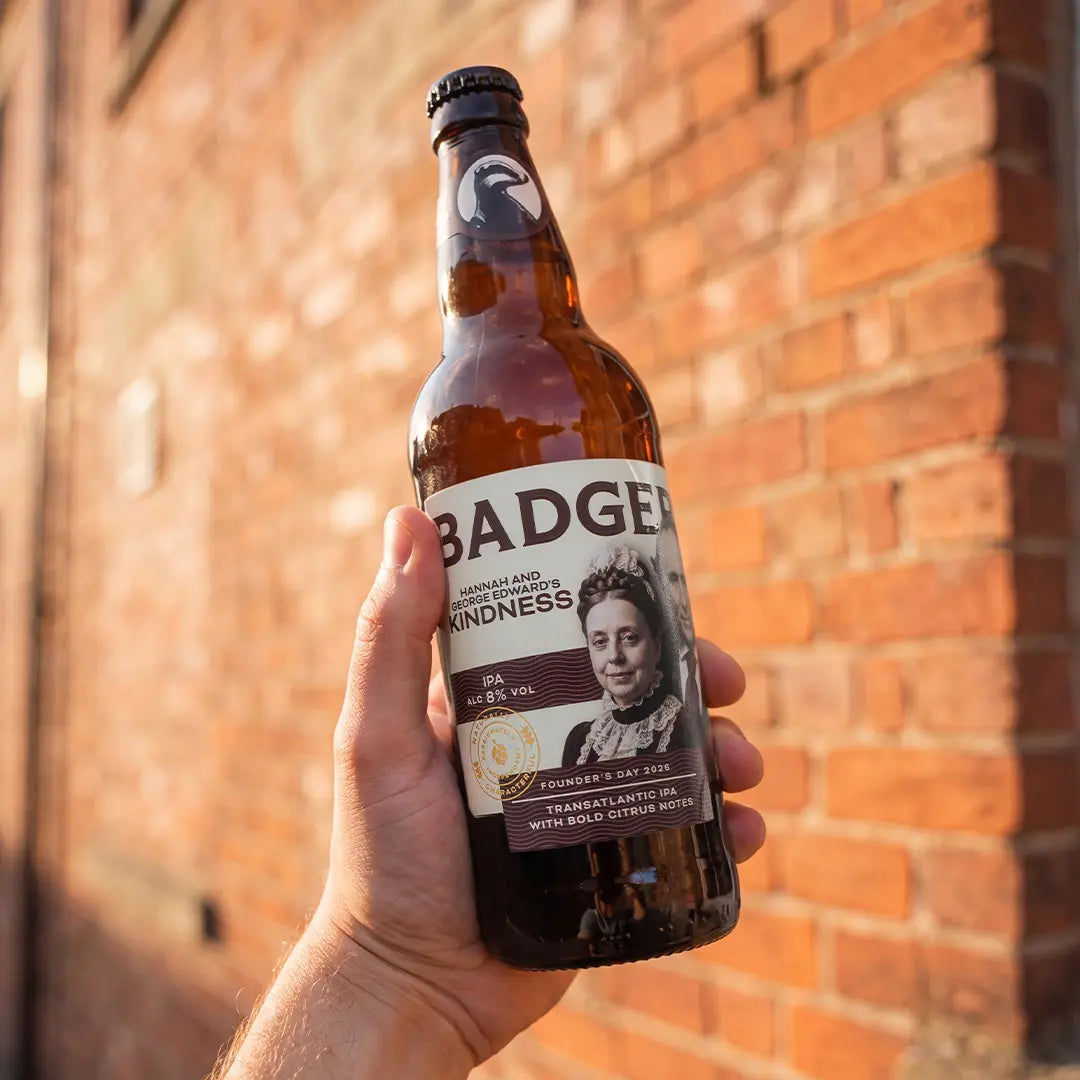Bottle of Hannah and George Edward's Kindness IPA held up against a brick wall