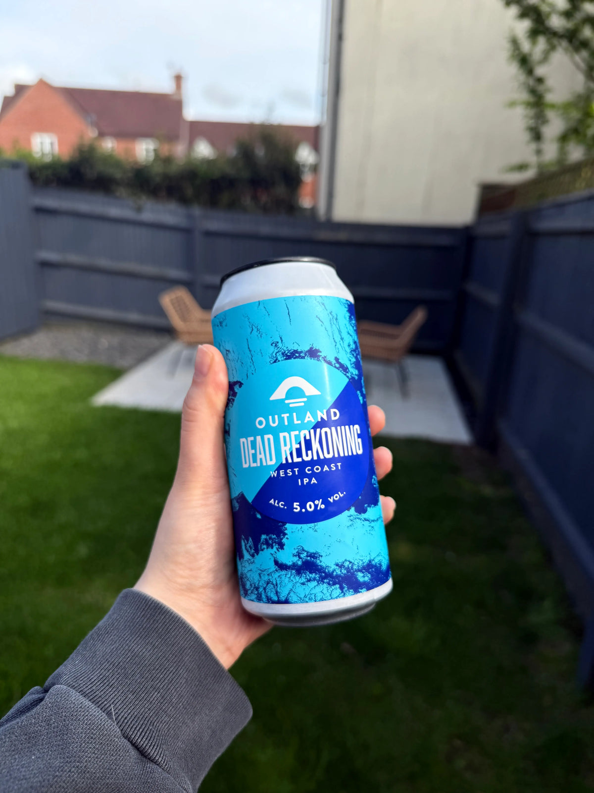 Hand holding a can of Outland Dead Reckoning in a garden