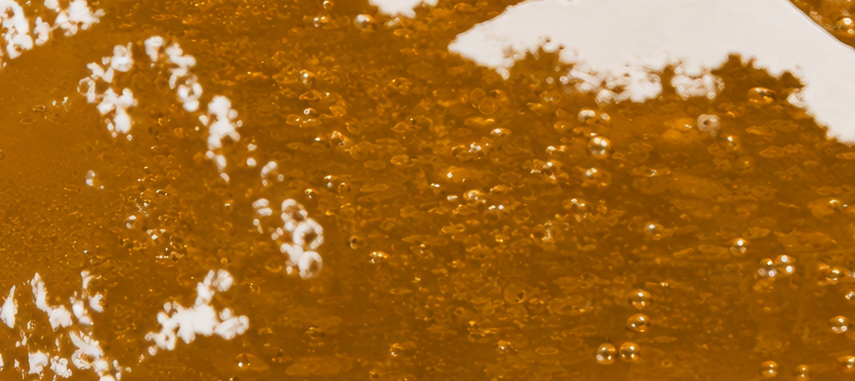 A close-up texture shot of Outland's East of Eden IPA beer liquid in an Outland pint glass, with small bubbles and bright white details.