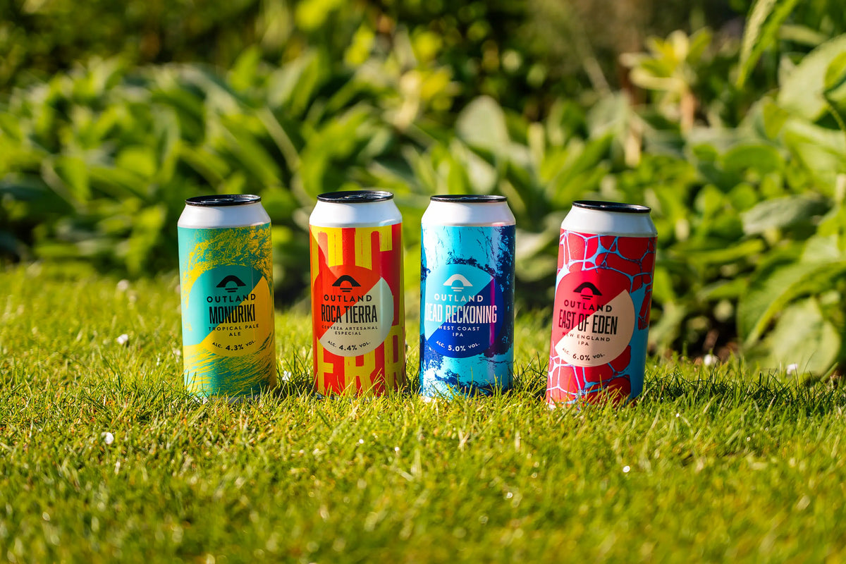 Four cans from the Outland range lined up on grass in front of garden planting