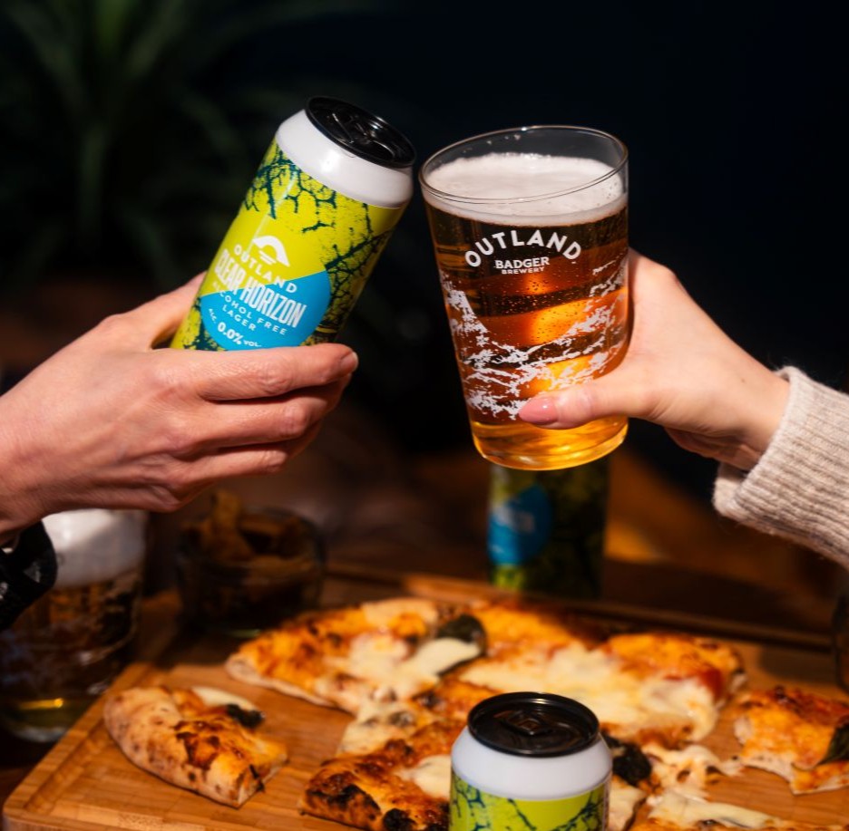 Two hands toasting with Outland Clear Horizon over a pizza board