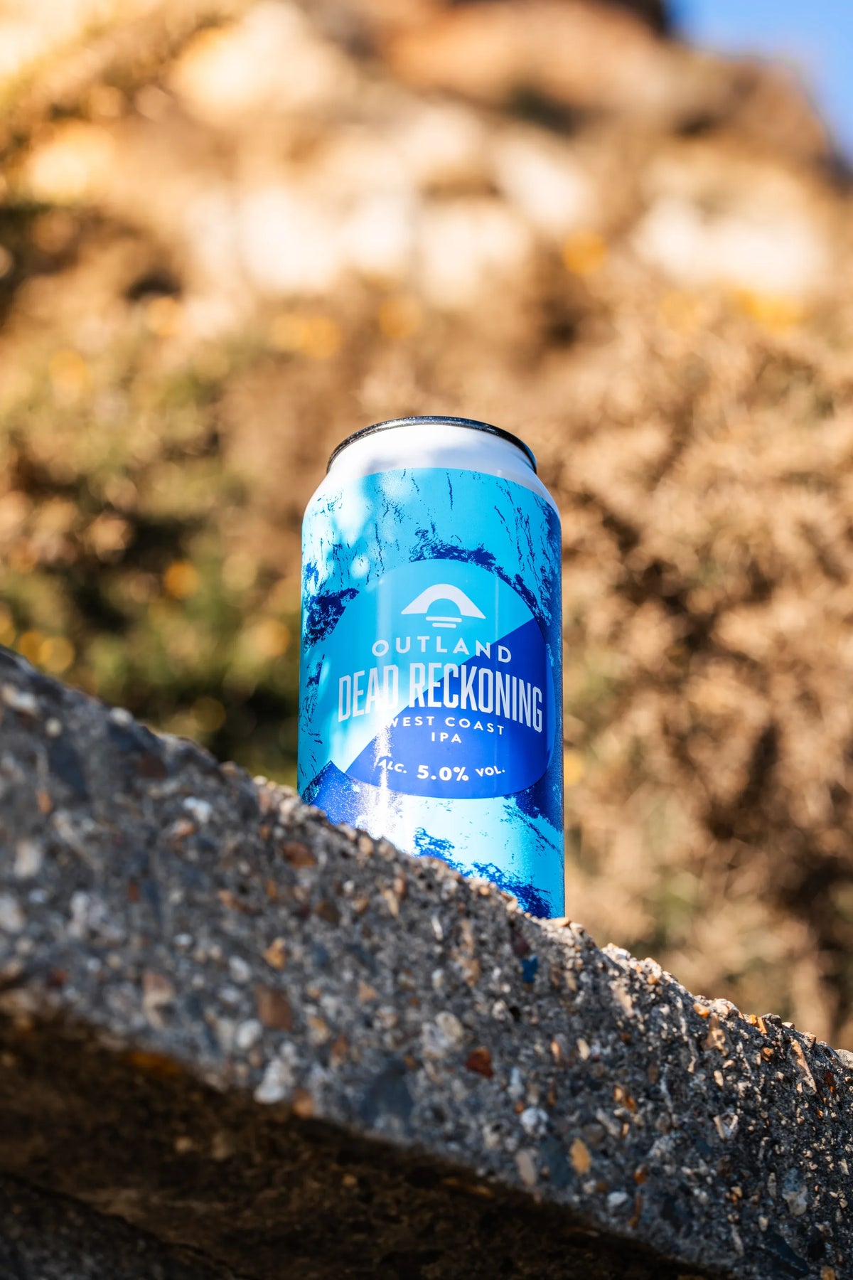 Can of Outland Dead Reckoning resting on a rock face on a sunlit clifftop walk