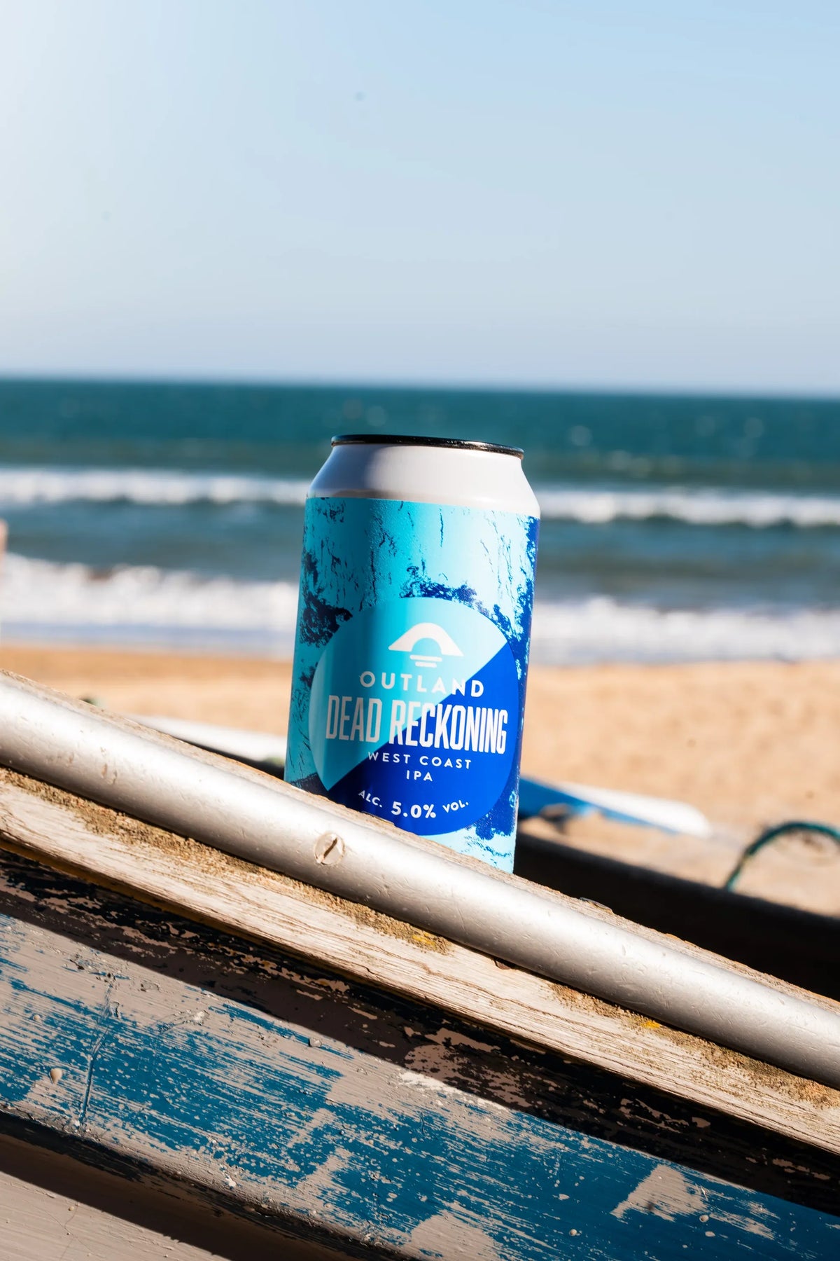 Can of Outland Dead Reckoning on a weathered railing overlooking the sea