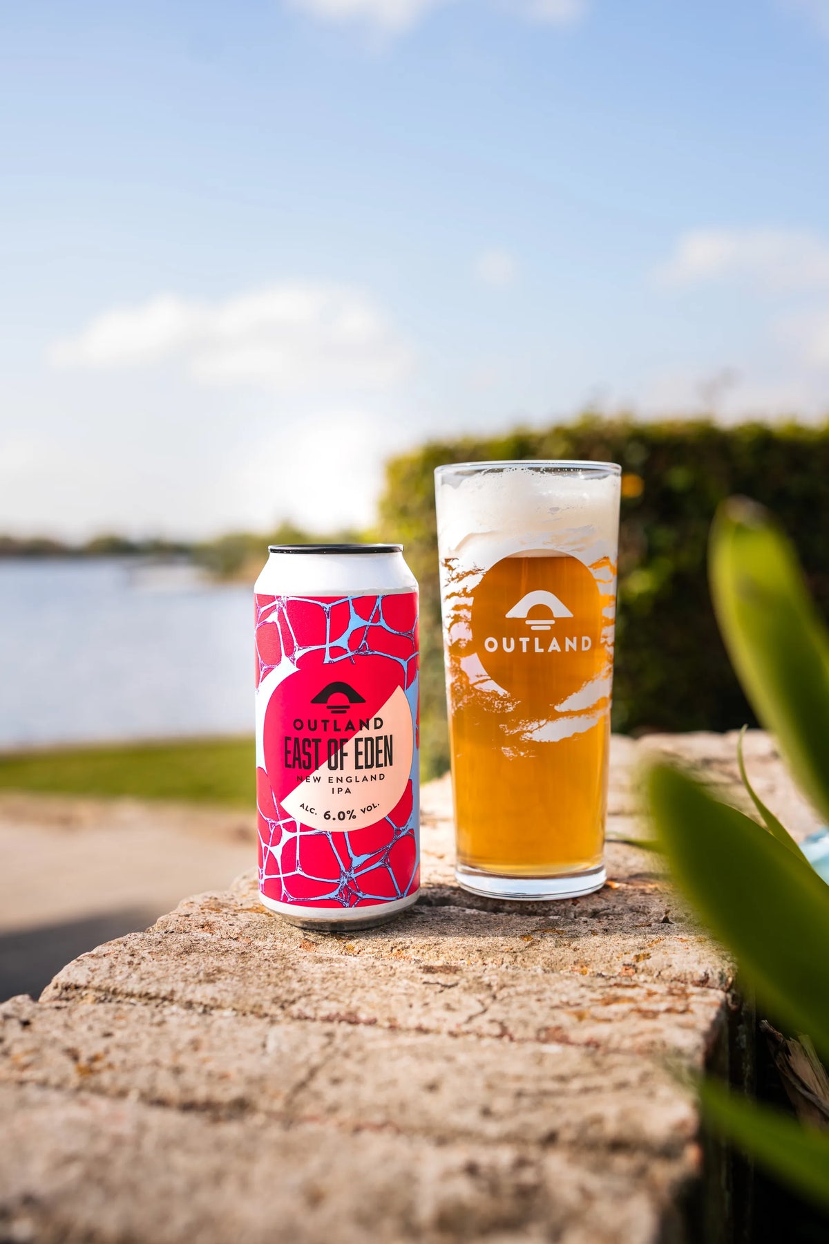 Cans of Outland East of Eden and a full glass on a rock with countryside behind