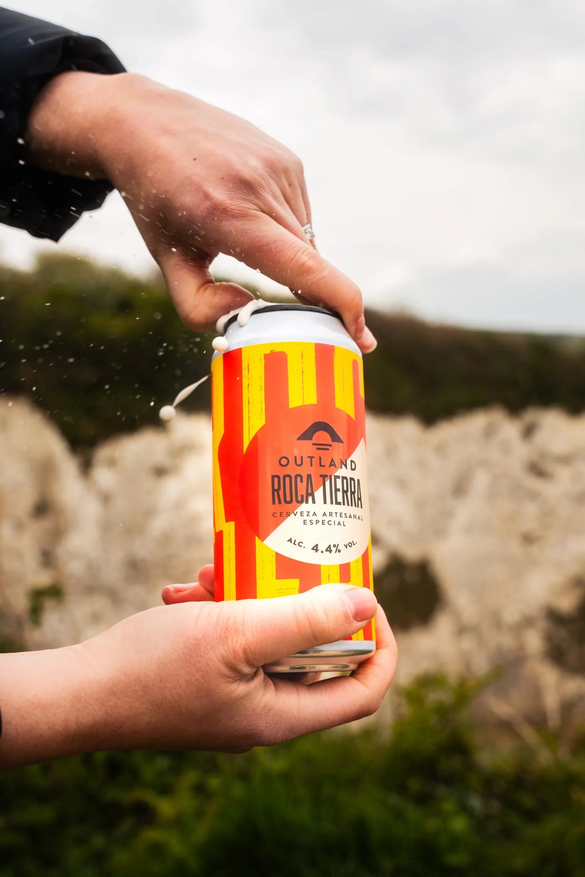 Hand holding a can of Outland Roca Tierra on a clifftop above Old Harry Rocks