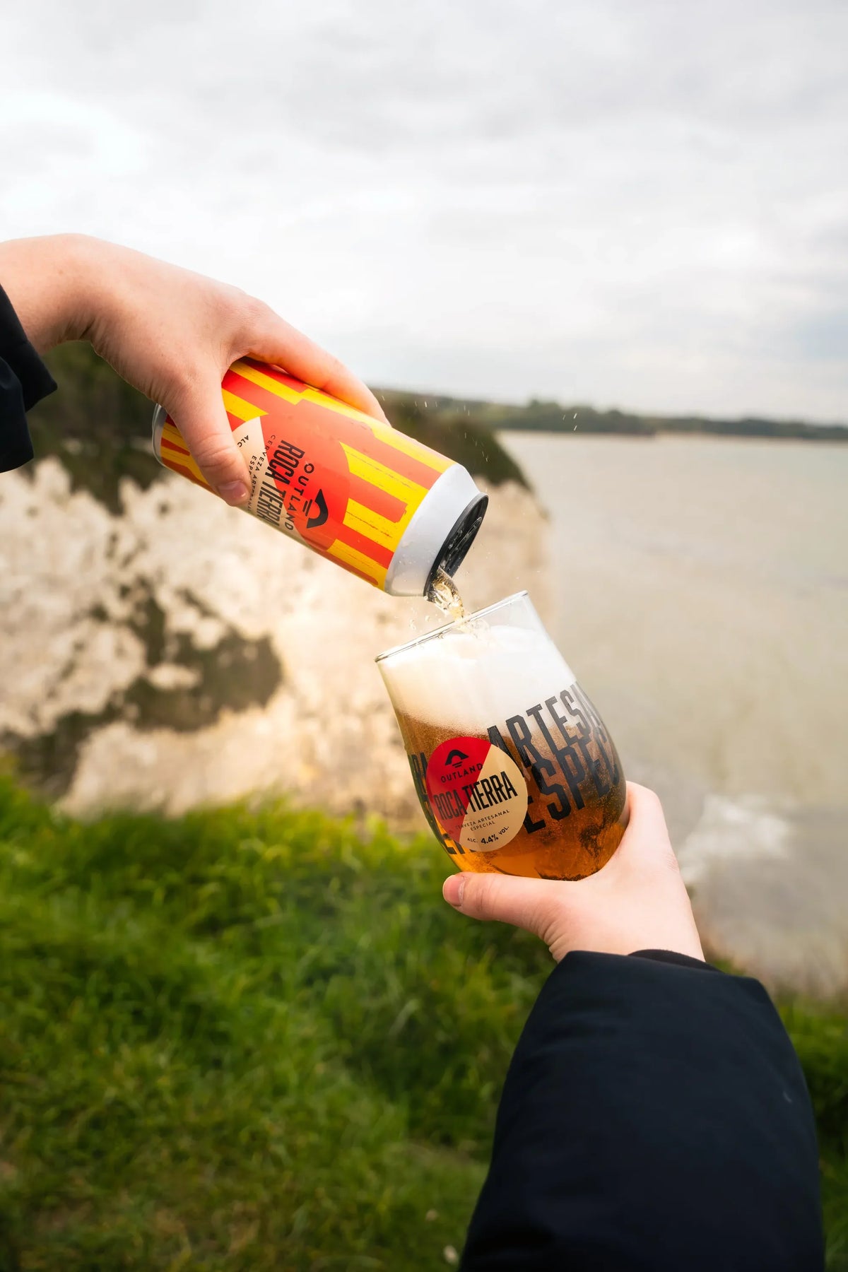 Outland Roca Tierra poured into a glass on a clifftop path above the sea