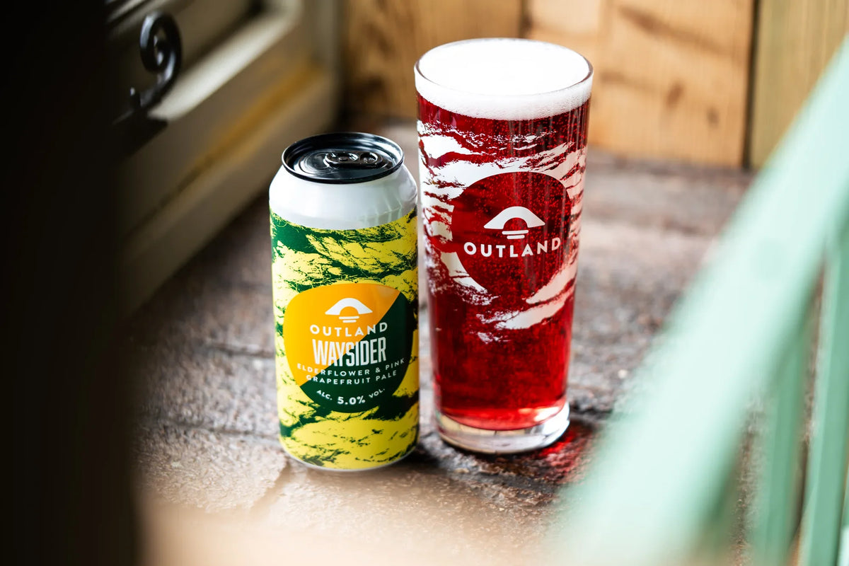 Cans of Outland Waysider and a full Outland pint on a wooden pub window ledge