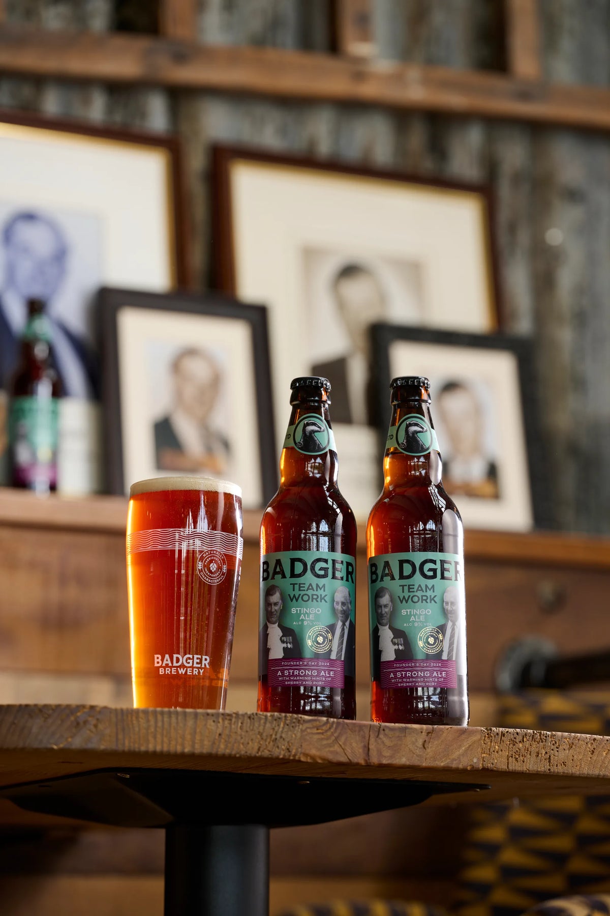 Bottles and glasses of Badger Teamwork on a table in front of framed family portraits