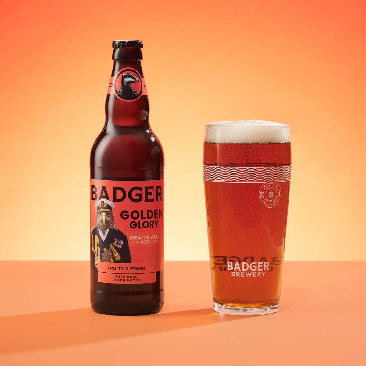 Bottle of Badger Golden Glory beside a full pint glass on a sunlit coral background