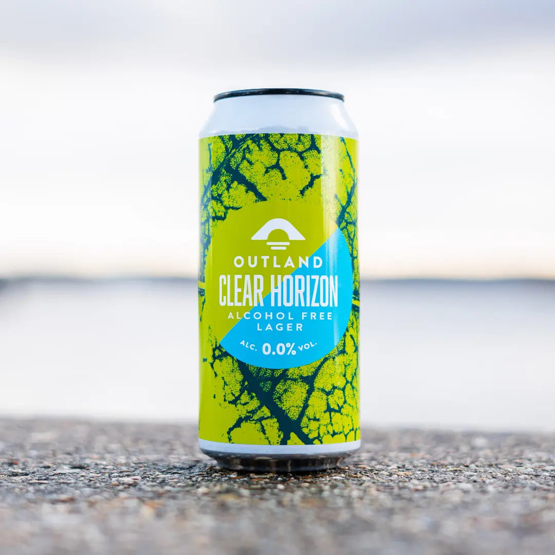 Can of Outland Clear Horizon 0.0% lager standing on a shingle beach