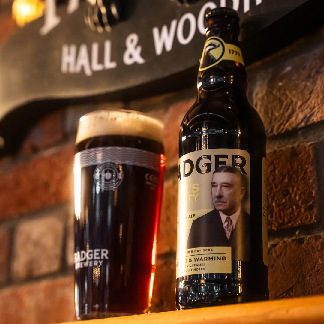 Bottle and dark pint of Frank's Integrity on a bar beneath a Hall & Woodhouse sign
