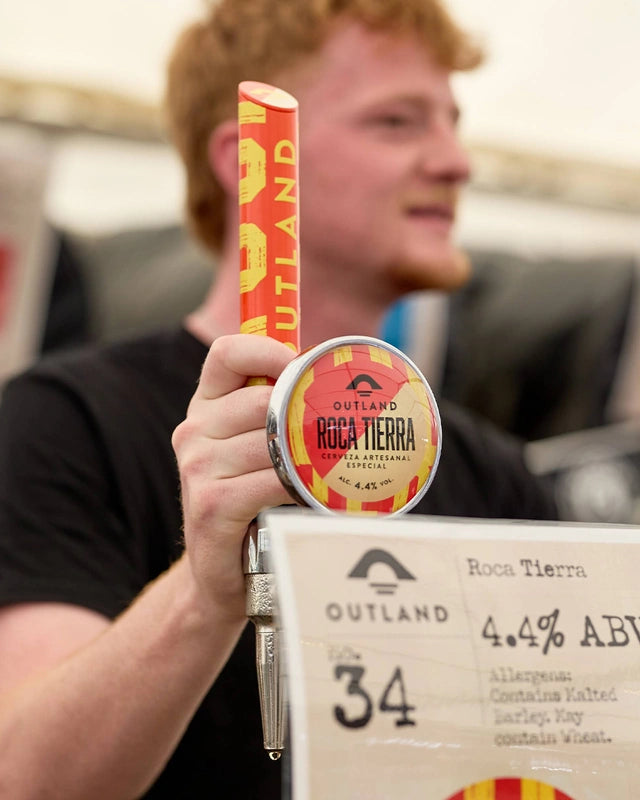 Man holding a can of Outland Roca Tierra at a beer festival stand