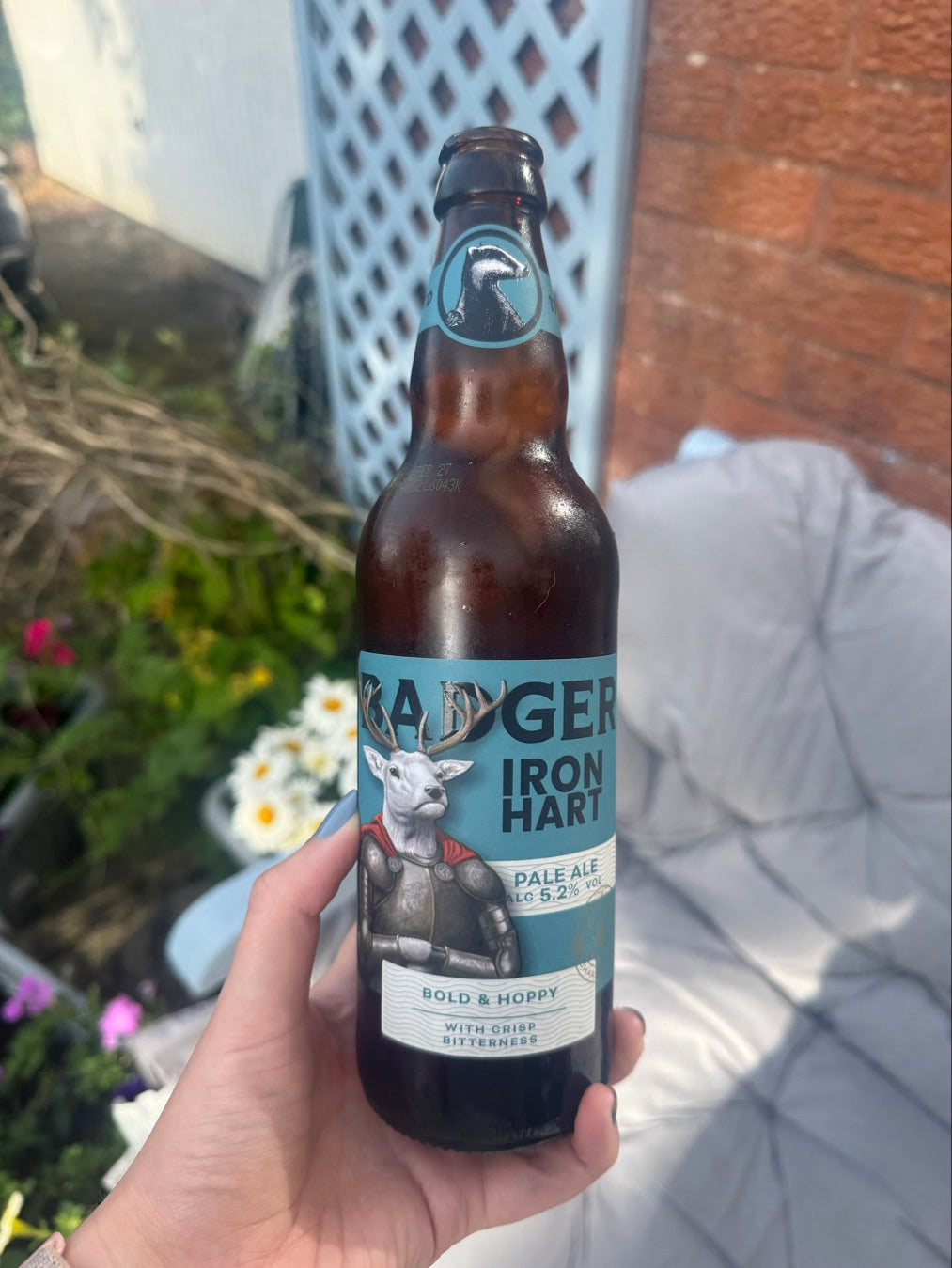 Hand holding a bottle of Badger Iron Hart in front of garden flowers