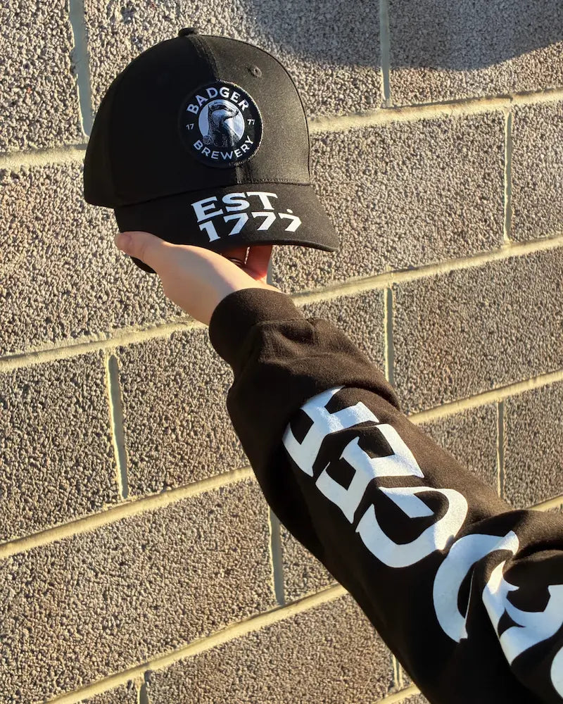 Close-up of the Est. 1777 embroidery on a Badger cap held to a brick wall