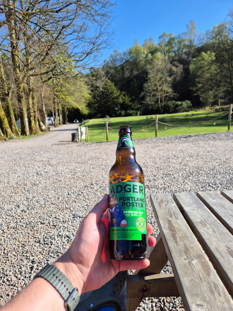 Hand holding a bottle of Badger Hopping Hare on a woodland path