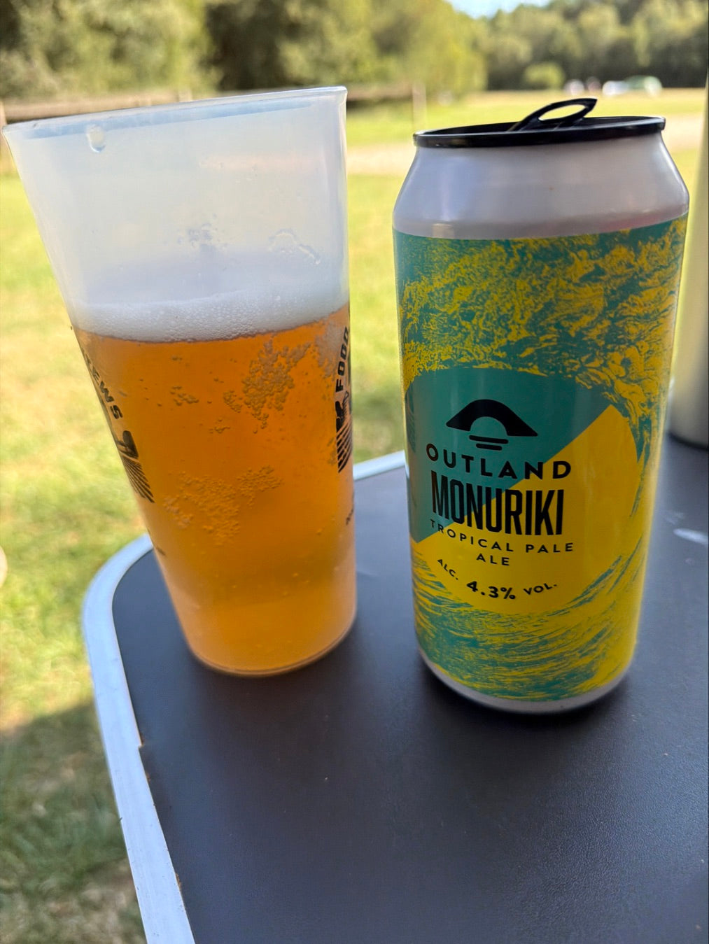 Glass of Outland Monuriki beside its can on a white outdoor table