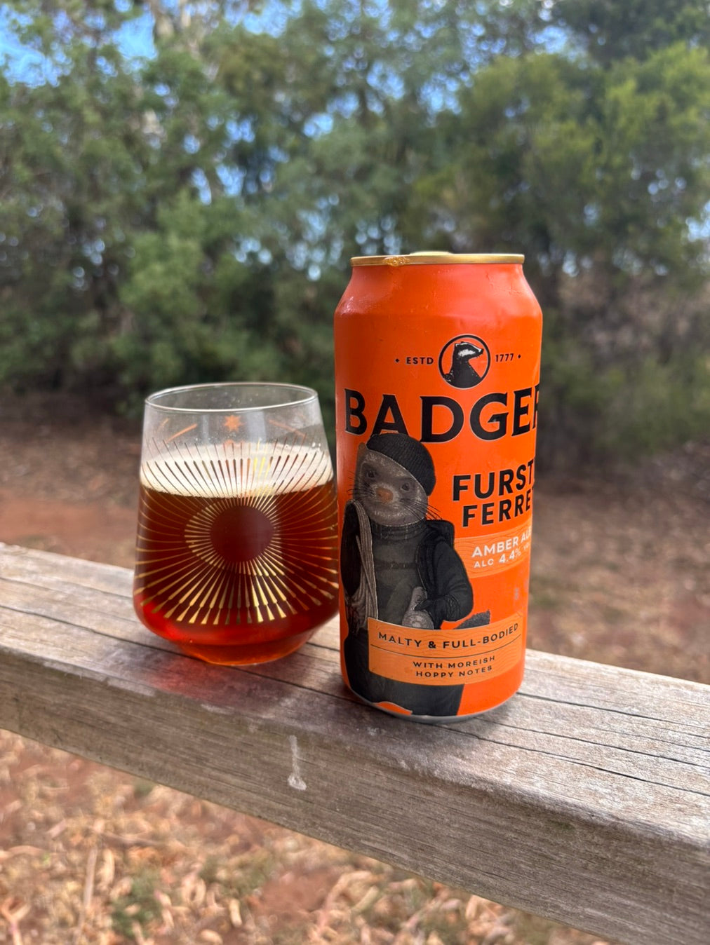 Can and glass of Badger Fursty Ferret on a wooden rail outdoors