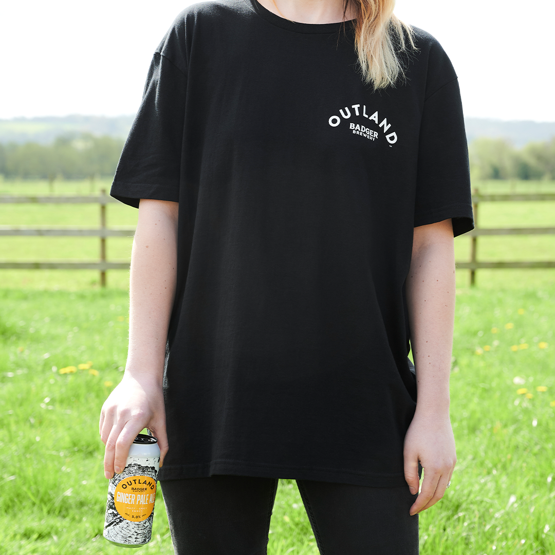 Person wearing Outland Black T-shirt (Front) with can of Outland Ginger Pale Ale