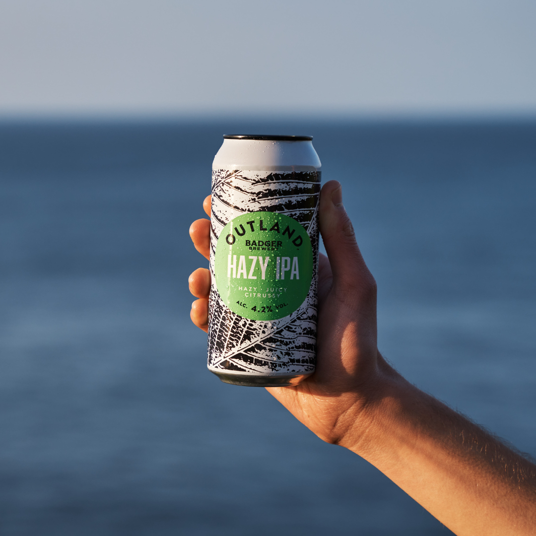 Person holding Outland Hazy IPA in front of sea