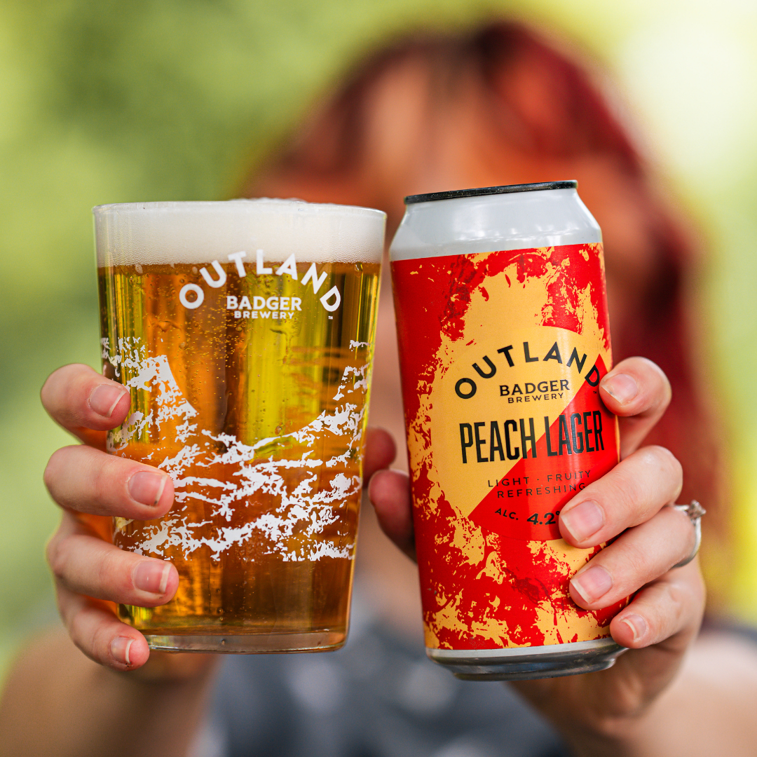 Person holding can and glass of Outland Peach Lager